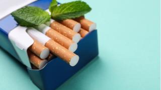 Pack of menthol cigarettes and mint on turquoise background, closeup.