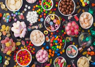 Pink lollipop candies in jar with various milk chocolate and jelly gums candies on black with liquorice allsorts and strawberry bonbons and large variety of sweets and candies.
