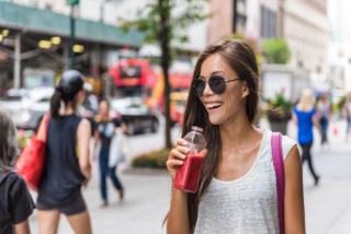 Urban city lifestyle hipster asian woman drinking healthy fruit vegetable berry juice smoothie walking on downtown street