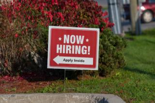 Outdoor lawn sign now hiring apply inside with direction arrow, selective focus. Great resignation, employment, understaffed business, work strikes, absent workers due to covid labor shortage concept.
