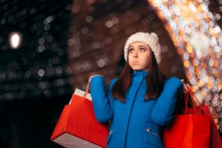 Tired Girl Holding Shopping Bags on Christmas Lights Decor. Exhausted stressed holidays buyer feeling fatigued