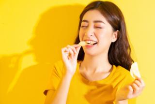 Smiling girl eating snack on yellow background