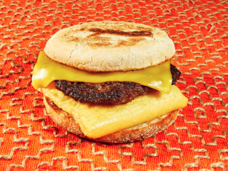 7-Eleven plant-based breakfast sandwich on an English muffin with two cheeses against and orange background.