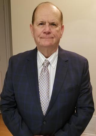 Dave Bryans in a blue suit standing against a beige wall