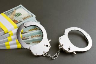 Hand cuffs and a pile of cash on a grey background.