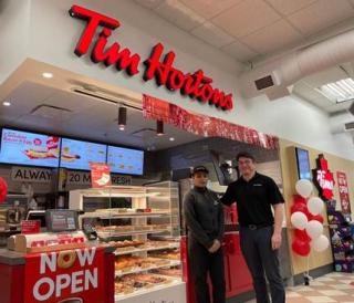 Two employees stand in front of a Tim Hortons kiosk at a Rabba location.