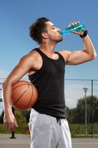 Young man drinking mineral water on a basketball court
