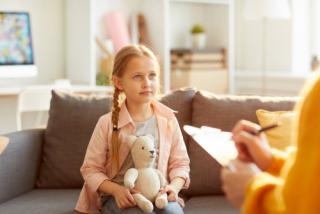 Portrait of cute little girl listening to psychologist during therapy session on youth issues, copy space