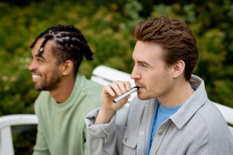 two men on a bench, one is vaping a silver Vuse ePod 2 e-cigarette
