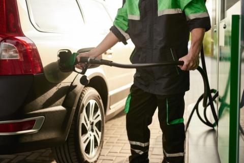 Unrecognizable man in uniform using hose with nozzle to refill tank of modern vehicle while working at gas station