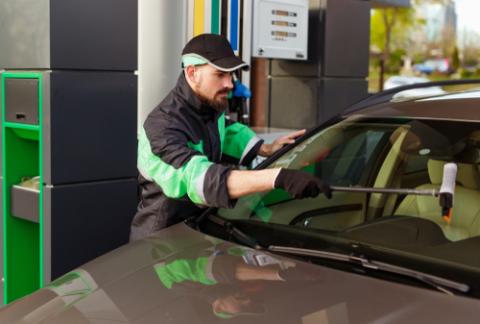 Bearded man in uniform cleaning windscreen of modern car while representing high quality service of filling station
