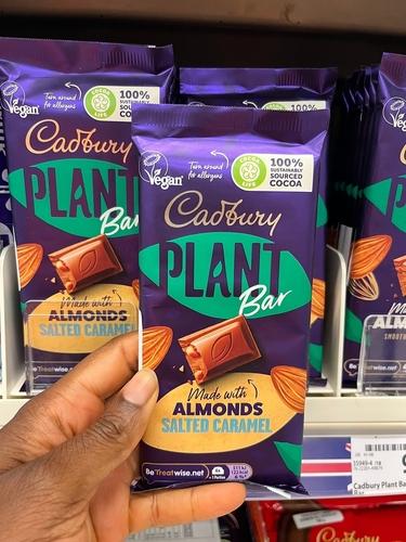 Black person holding a Cadbury plant-based, sustainably sourced flavoured chocolate bar in a grocery store