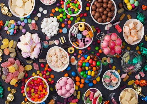 Pink lollipop candies in jar with various milk chocolate and jelly gums candies on black with liquorice allsorts and strawberry bonbons and large variety of sweets and candies.