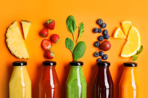 Flat lay composition with bottles of delicious juices and fresh ingredients on orange background