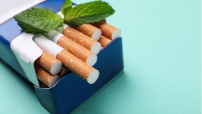 Pack of menthol cigarettes and mint on turquoise background, closeup.