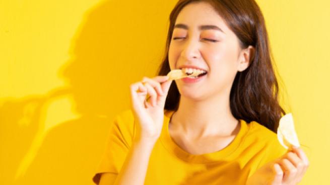 Smiling girl eating snack on yellow background