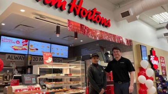 Two employees stand in front of a Tim Hortons kiosk at a Rabba location.