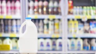 Milk bottle in a supermarket on background blurred beverage, milk showing on shelves in the cold freezer.