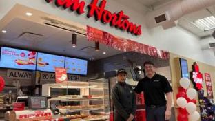 Two employees stand in front of a Tim Hortons kiosk at a Rabba location.