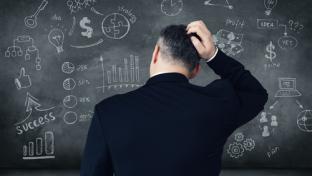 confused man looks at black board with chalk drawings of charts and numbers