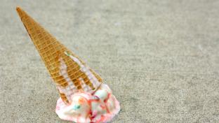 A rainbow colored ice cream cone has dropped upside down on the sidewalk on a summer day